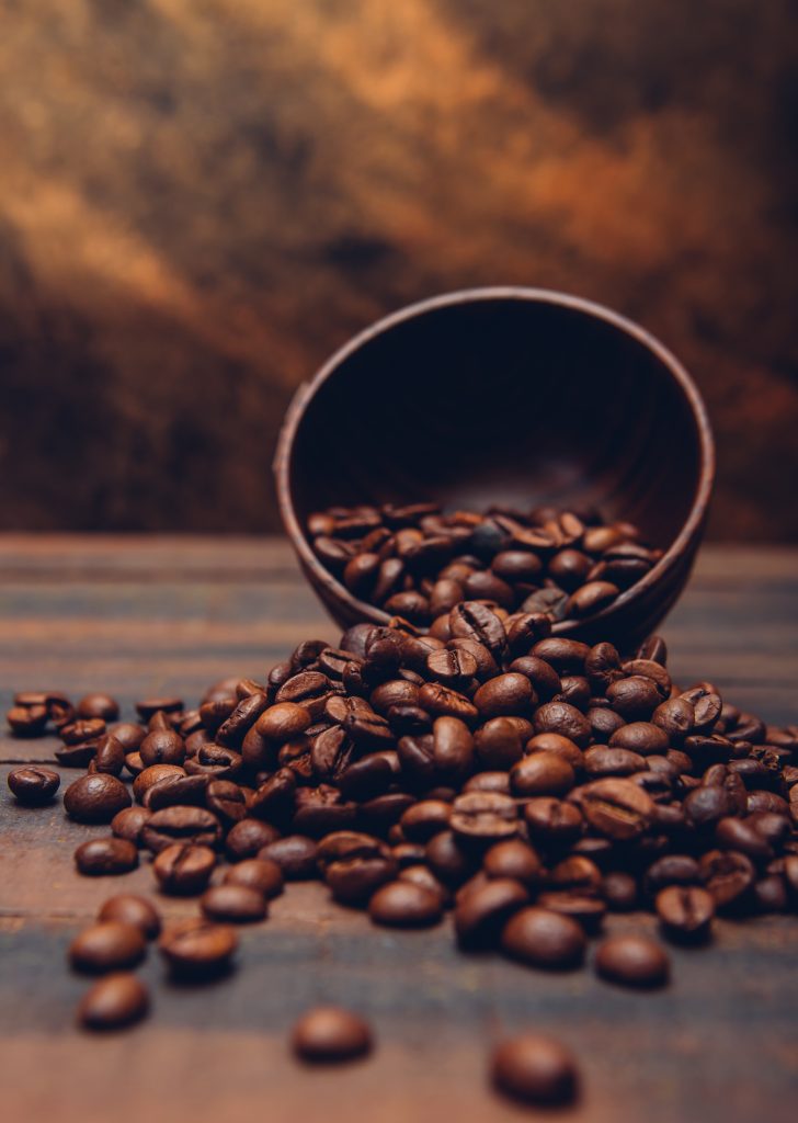 Uma tigela de madeira virada, com grãos de café escuros espalhados ao redor.